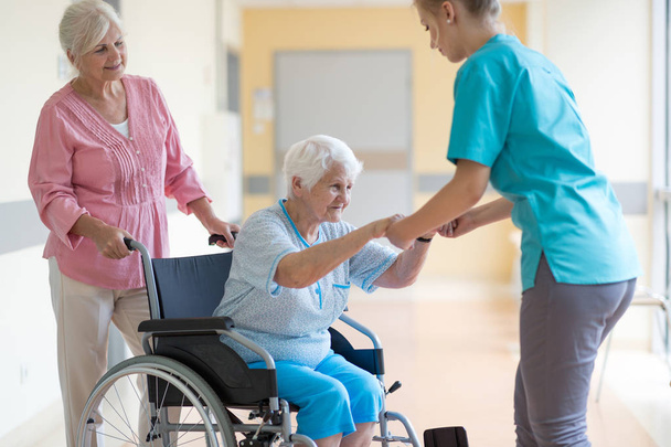 Femme âgée en fauteuil roulant avec sa fille et son infirmière
 - Photo, image