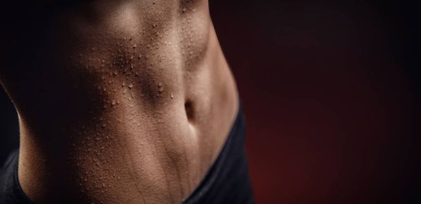 Closeup of drop of sweat on skin abdomen woman after workout. Dark background - Foto, Imagem