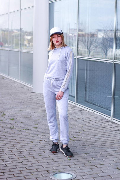 The girl is blonde in a gray sports suit. Street clothing. Sport - Foto, Bild