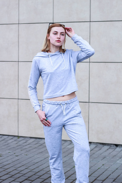 The girl is blonde in a gray sports suit. Street clothing. Sport - Zdjęcie, obraz