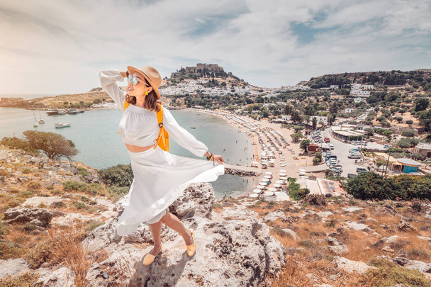 glückliche asiatische Frau reist in Griechenland. Spaß am atemberaubenden Blick auf den Badeort und die Altstadt von Lindos auf dem Berg - Foto, Bild