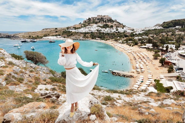 Счастливая азиатка путешествует по Греции. Развлекаясь на потрясающий вид на морской курорт и старый город Линдос на горе
 - Фото, изображение