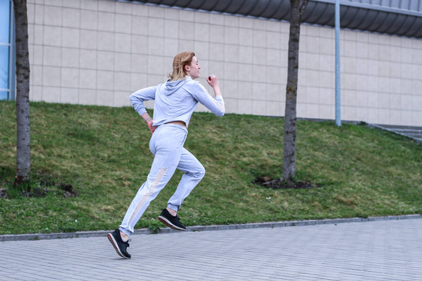 The girl is blonde in a gray sports suit. Street clothing. Sport - Fotoğraf, Görsel