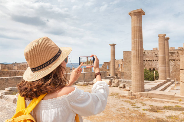 Tourist girl taking photos and selfie of tourist landmark of ancient Acropolis town. Travel destinations and sightseeing tours - Foto, Bild