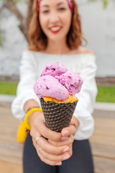 Азиатка ест большое мороженое с черничным вкусом на открытом воздухе
 - Фото, изображение