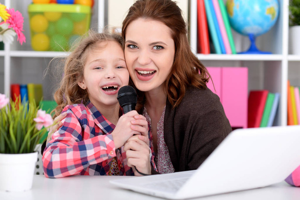 Emocional madre e hija cantando karaoke con portátil en casa
 - Foto, imagen