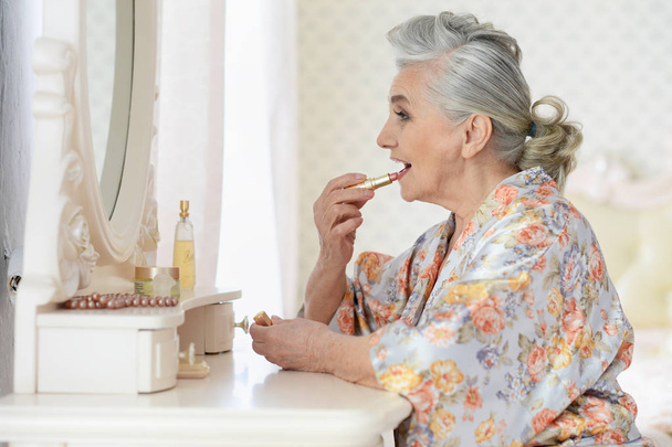 portrait of happy senior woman applying makeup near dressing table - Φωτογραφία, εικόνα