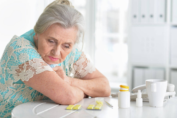 Sad sick senior woman sitting at table with pills - Фото, изображение