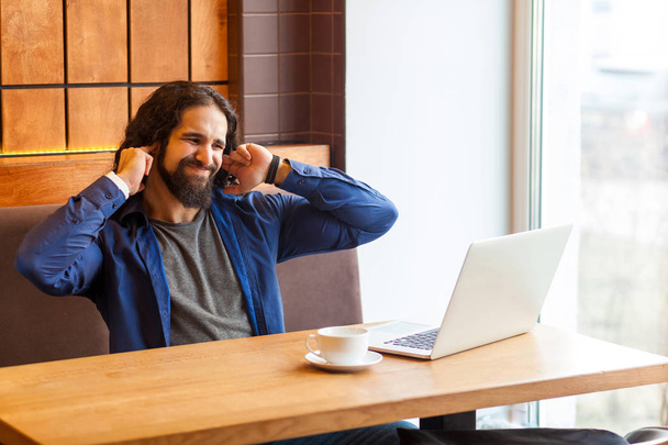 annoyed young adult man freelancer in casual style closed ears with fingers while sitting in cafe and talking with friend in laptop, lifestyle concept - Photo, image