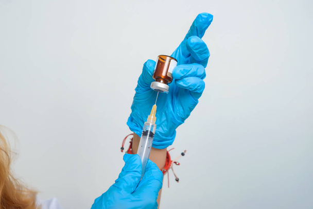 Ärztin füllt Spritze mit Medikamenten. Verfahren in der Arztpraxis. Krankenschwester in blauen Latex-Handschuhen. - Foto, Bild