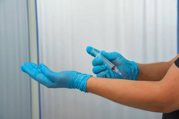 Guy in blauwe latex handschoenen houden van een spuit. Een man maakt zichzelf een vaccin. Een schot in de arm. - Foto, afbeelding
