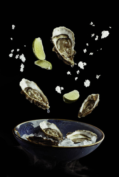 flying oysters with lime and ice out of plate. Concept of food preparation in low gravity mode, food levitation. Separated on black background. High resolution image - 写真・画像