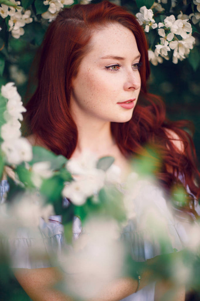 Model with red hair posing in a blooming apple tree. - Fotografie, Obrázek