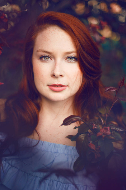 Model with red hair posing in a blooming apple tree. - Foto, Imagem