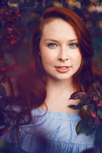Model with red hair posing in a blooming apple tree. - Fotó, kép