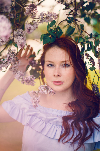The red-haired model poses in the summer in a dress of blooming lilacs. - 写真・画像