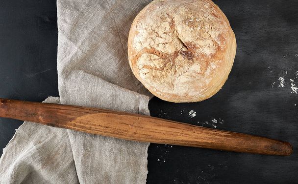 okrągły wypiekany chleb i drewniany stary wałek na czarnym stole - Zdjęcie, obraz