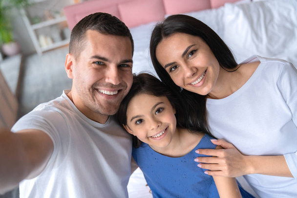 Счастливый молодой человек делает селфи со своей семьей. Семья стоит в спальне и делает селфи дома
 - Фото, изображение