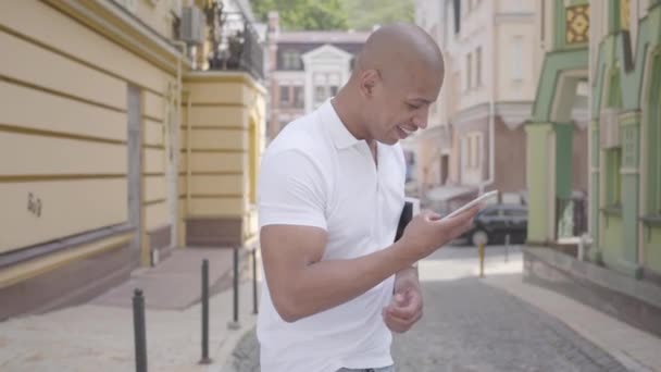 Portrait of handsome successful confident bald middle eastern man typing on the cell phone standing on the street in front of old buildings looking around. Professional skills. - Video, Çekim