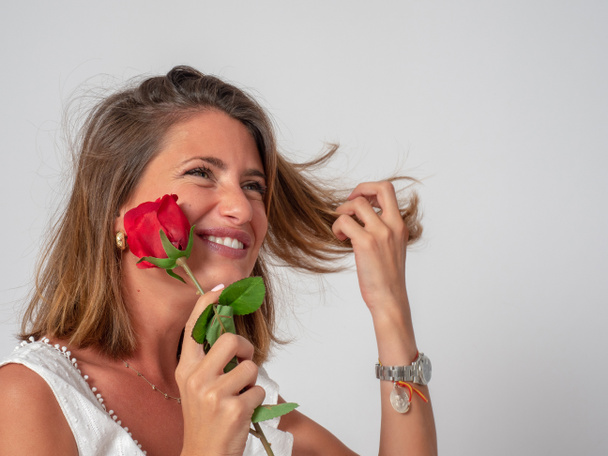 speelt, aanraakt en ruikt een rode roos in een fotografische Studio - Foto, afbeelding