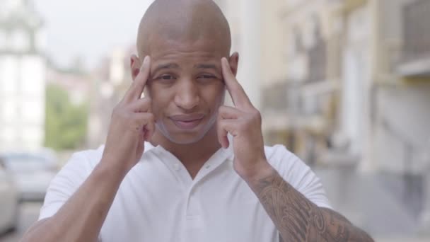 Portrait of attractive bald middle eastern man standing in the city street massaging his forehead with fingers. The guy is tired and stressed, he has headache. Intensive city lifestyle. Slow motion. - Filmmaterial, Video