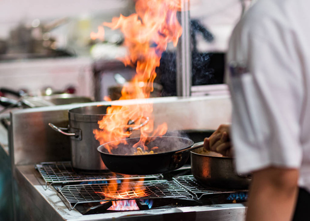 Кухар готує з полум'ям на сковороді на кухонній плиті
 - Фото, зображення