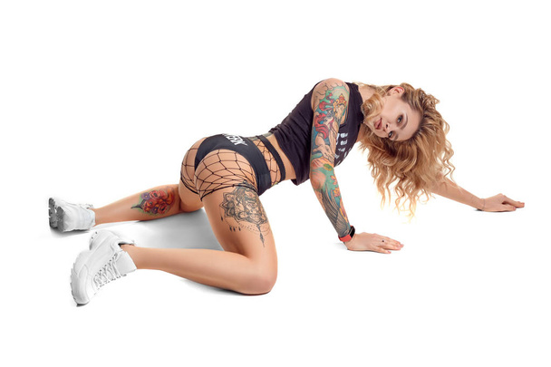 Sexy blond twerk woman with tattoed body and long curly hair is posing in studio. - Photo, Image
