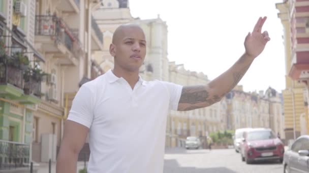 Portrait of handsome confident bald middle eastern man raising his hand to catch a taxi on the street of the old city. Leisure of the city dweller. Slow motion - Záběry, video