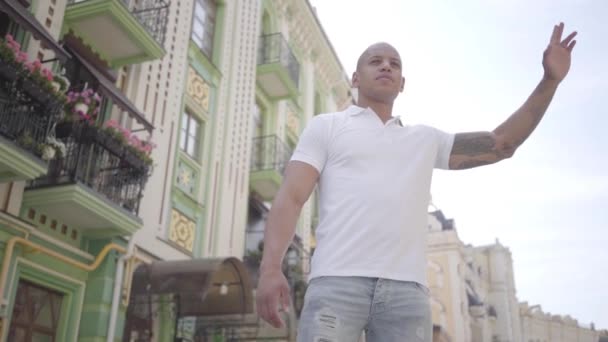 Portrait of confident bald middle eastern man raising his hand to catch a taxi on the street of the old city. Leisure of the city dweller. Slow motion. - Video