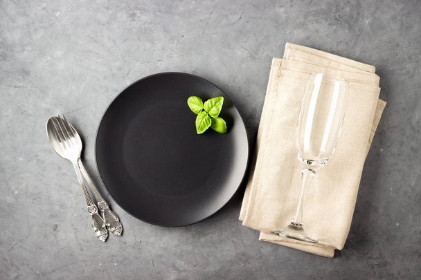 Table setting with black matte plate, wine glass and cutlery. View from above over gray concrete background. - Photo, image