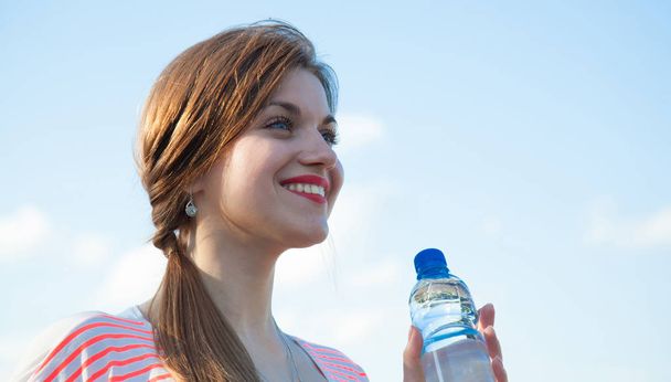 Puur water voor een gezonde en actieve levensstijl. Gelukkig lachende jonge vrouw met fles drinkwater buiten - Foto, afbeelding