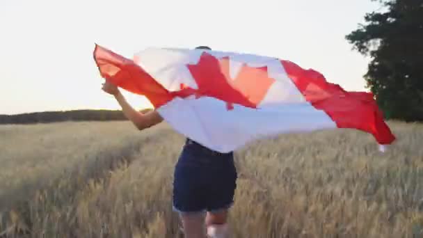 На заході сонця молода канадійка біжить з прапором Канади над пшеничним полем. - Кадри, відео