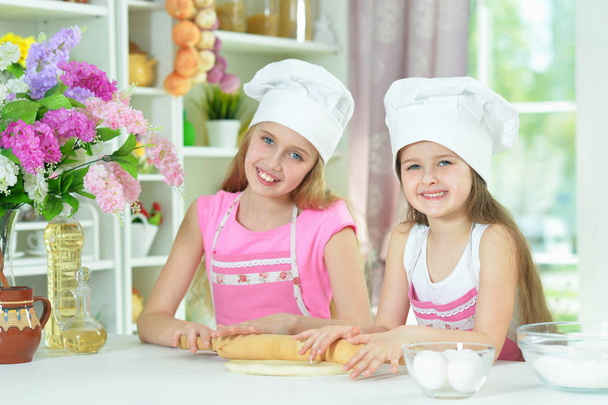 Cute little girls in chefs hats making dough in the kitchen  at home - Photo, image