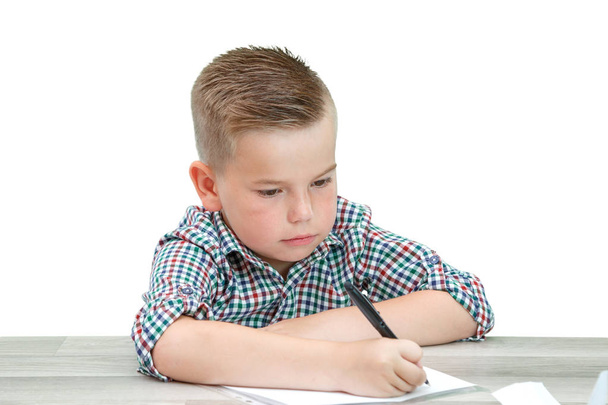 Caucasian school-age boy in a plaid shirt sitting at the table a - Zdjęcie, obraz