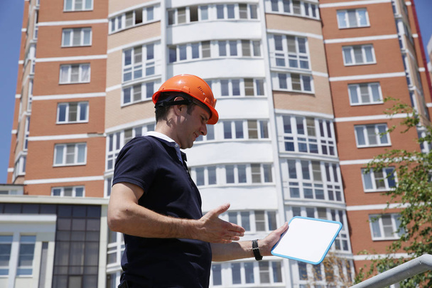 Portrait of a young man in a protective helmet with a tablet for writing in hand with copy space for text and image in front of a tall building. Business, architecture and construction. - Photo, Image