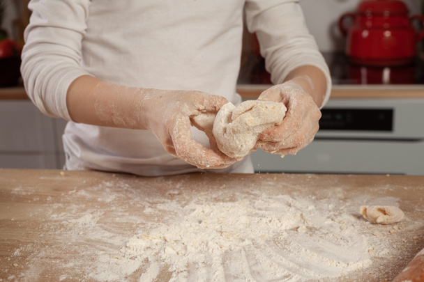 Ένα όμορφο κοριτσάκι ντυμένο με άσπρη μπλούζα φτιάχνει ζύμη για να ψήνεις ψωμί στην κουζίνα.. - Φωτογραφία, εικόνα