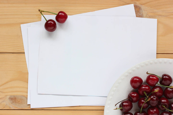 clean sheets of white paper on the table and a plate of cherries - Фото, зображення