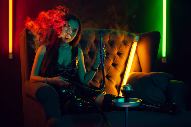 Sexy brunette model is het roken van een waterpijp uitademen van een rook in een luxe nachtclub. - Foto, afbeelding