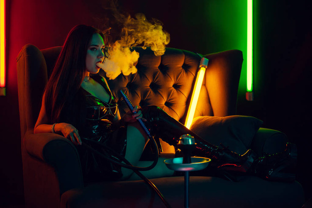 Sexy modelo morena está fumando una cachimba exhalando un humo en un club nocturno de lujo
. - Foto, imagen
