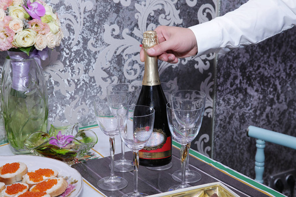  de hand van een man houdt een fles champagne op een tafel met een glazen broodjes met rode kaviaar - Foto, afbeelding