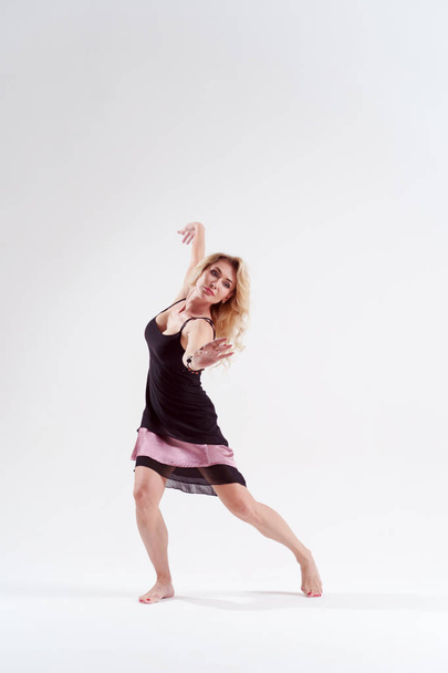 Image of dancing blonde looking to side in black dress in studio - 写真・画像