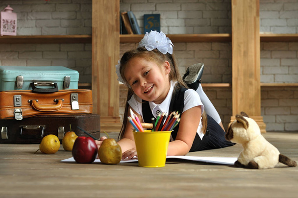 Roztomilá holka ve školní uniformě s bílými luky. leží na podlaze a kreslí barevnými tužkami - Fotografie, Obrázek