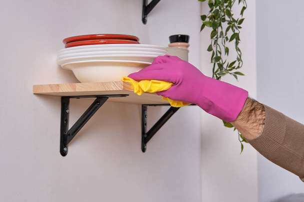 Joven guapo manos fuertes en guantes de color rosa limpia el estante por encima de la superficie de cocción con detergentes, vista de cerca
 - Foto, Imagen