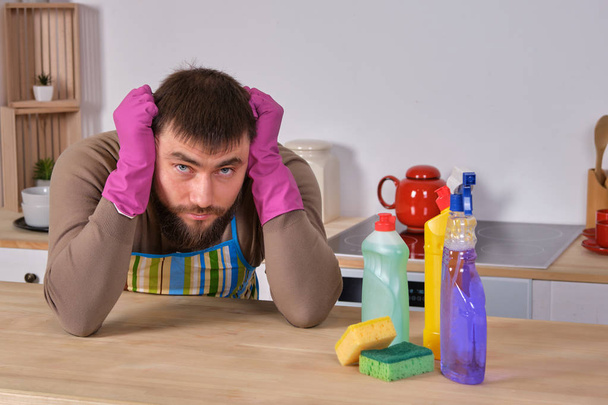 Young man wanted to help his wife in housecleaning, but he doesnt know what to do with all of detergents - Photo, Image