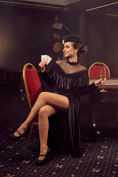 Young wonderful woman is posing sitting on a chair against a poker table in luxury casino. - 写真・画像