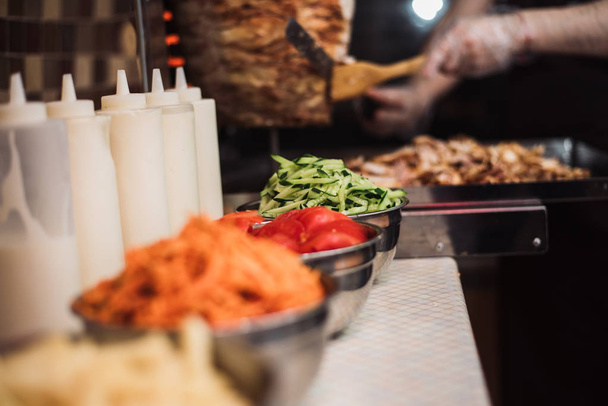 Getränke mit Tomaten, Gurken, koreanischen Karotten und Pommes frites, Saucengerichte auf dem Hintergrund von Spießen und gebratenem Hühnerfleisch für Shawarma. - Foto, Bild