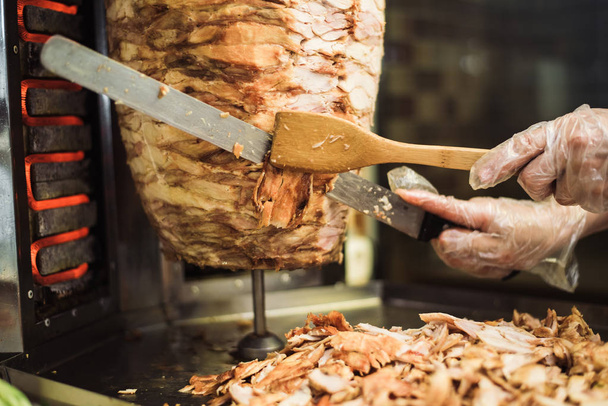 Cooking shawarma and ciabatta in a cafe. A man in disposable gloves cuts meat on a skewer. - Photo, image