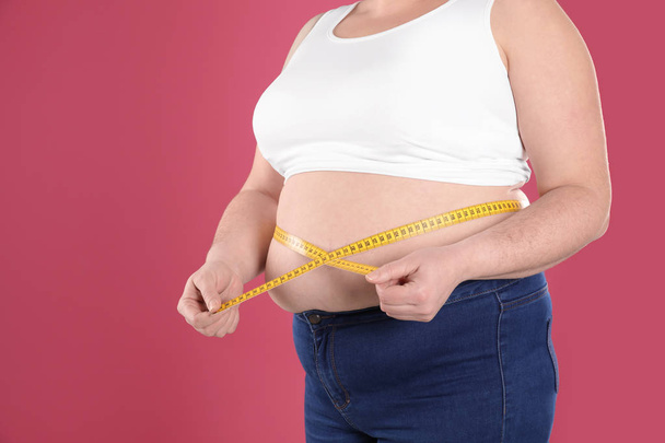 Overweight woman measuring waist with tape on color background, closeup. Space for text - Photo, image