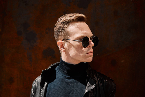 portrait of a handsome young man in sunglasses on a rusty iron background - Valokuva, kuva
