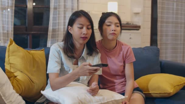 Lesbian lgbt women couple watching television at home, Asian female lover feeling happy funny moment looking drama entertainment together on sofa in living room in night concept. - Imágenes, Vídeo